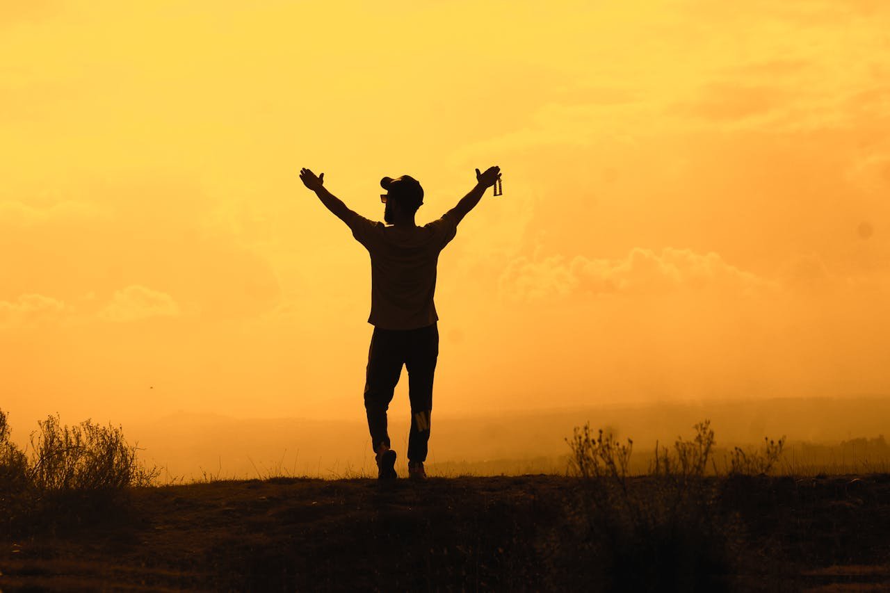 A silhouette of a man raising his hands in celebration against a vibrant sunset sky, symbolizing triumph and freedom.